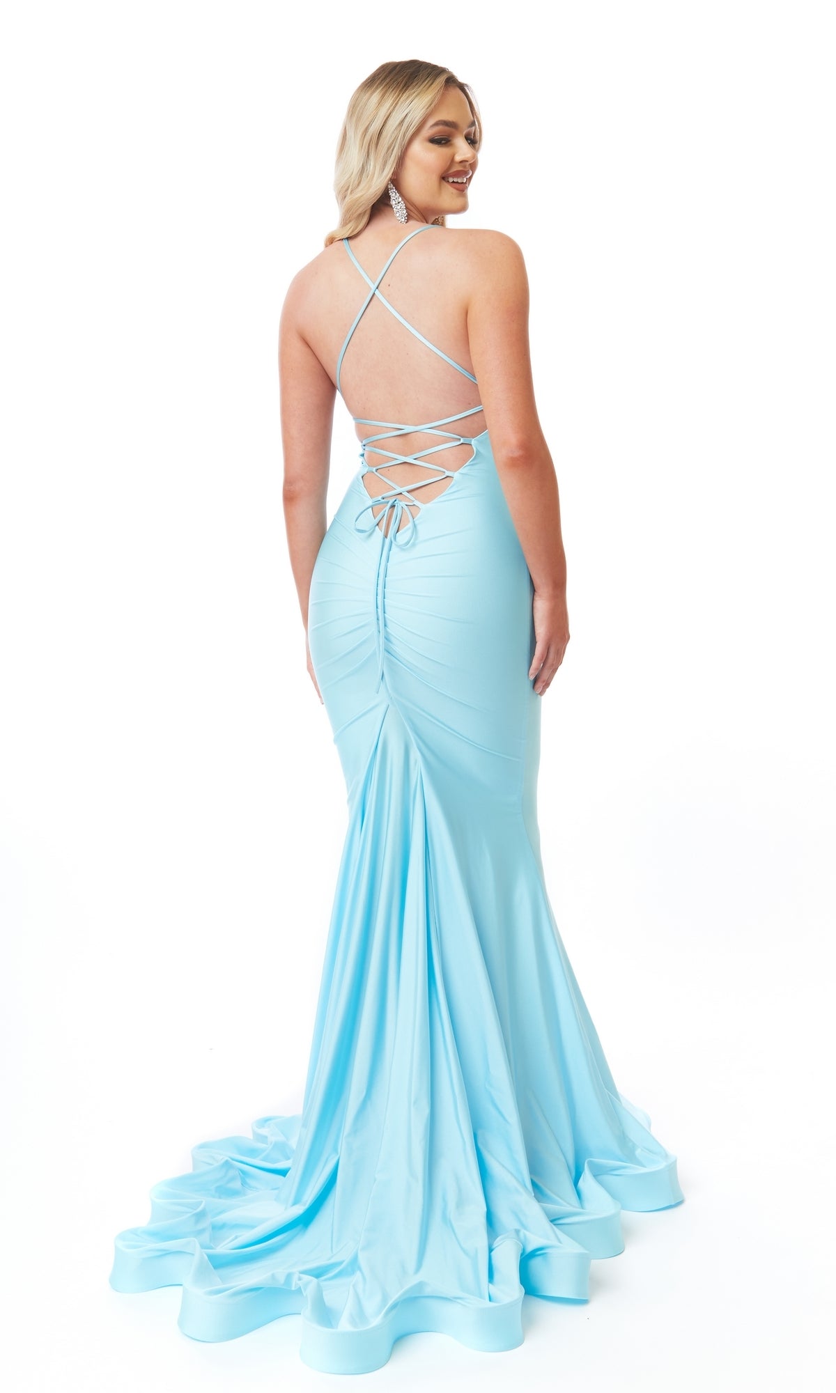 Wearing the Lace-Up Open-Back Long Prom Dress: Atria 6557H, a woman poses, smiling over her shoulder. The light blue, floor-length dress features a mermaid skirt and lace-up open back against a white background.